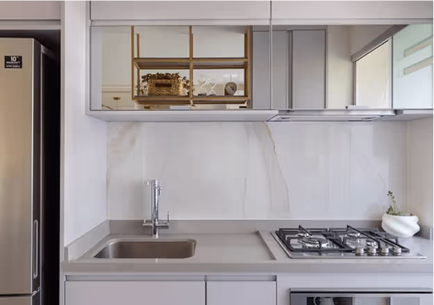 Cozinha moderna pequena com armários cinza, pia inox, fogão a gás embutido e geladeira inox.