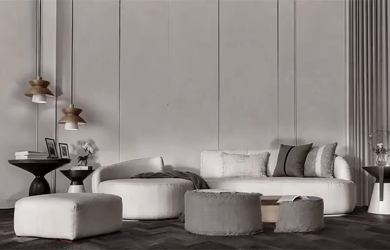 Sala de estar minimalista com sofá branco curvo, almofadas cinza e mesa de centro com pufes em tons neutros.