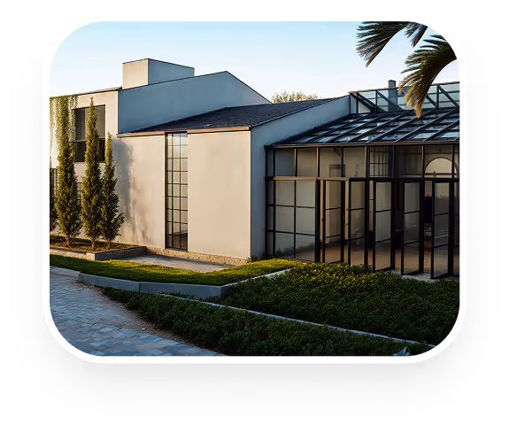 Casa moderna branca com grandes janelas de vidro e jardim bem cuidado com árvores altas.