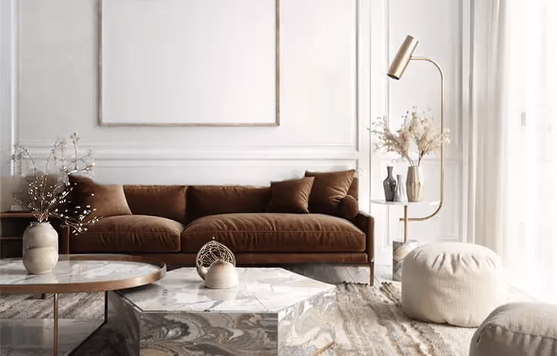 Sala de estar moderna com sofá marrom, duas mesas de centro de mármore, pufe branco, luminária dourada e vaso com flores secas.